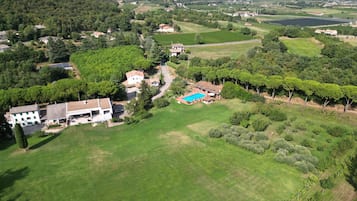 An aerial view of a residential area with houses, a swimming pool, and surrounding greenery.