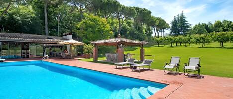 A swimming pool with lounge chairs and a pergola on a brick patio.