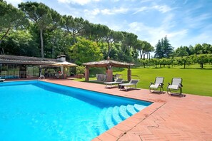 A swimming pool with lounge chairs and a pergola on a brick patio.