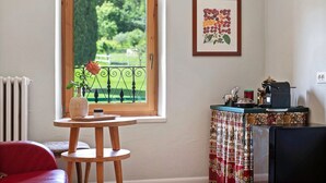 A room with a window, a radiator, a table with a vase, a red chair, a patterned curtain, and a framed picture on the wall. - Cavallina Retreat - Guest House with Private Pool, Garden, and Wi-Fi (Affi)