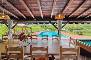 An outdoor dining area with a pool, wooden chairs, and a table with a vase of flowers.