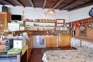 A compact kitchen with a built-in oven, a refrigerator, and a sink. There are wooden cabinets and a brick wall.