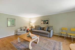 A living room with a sofa, two chairs, a coffee table, a rug, and artwork on the walls.