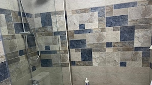 Ducha con cerramiento de vidrio, cabezal de ducha de mano y grifo de mano.