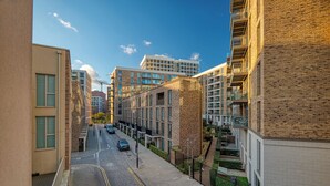 A modern urban street with multi-story buildings, a clear sky, and a few cars on the road. - Austin David Royal Wharf  (London)