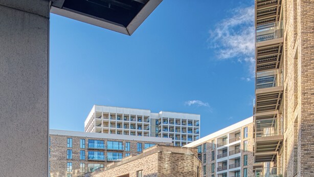 A modern apartment building with a view of a street and parked cars. - Austin David Royal Wharf  (London)