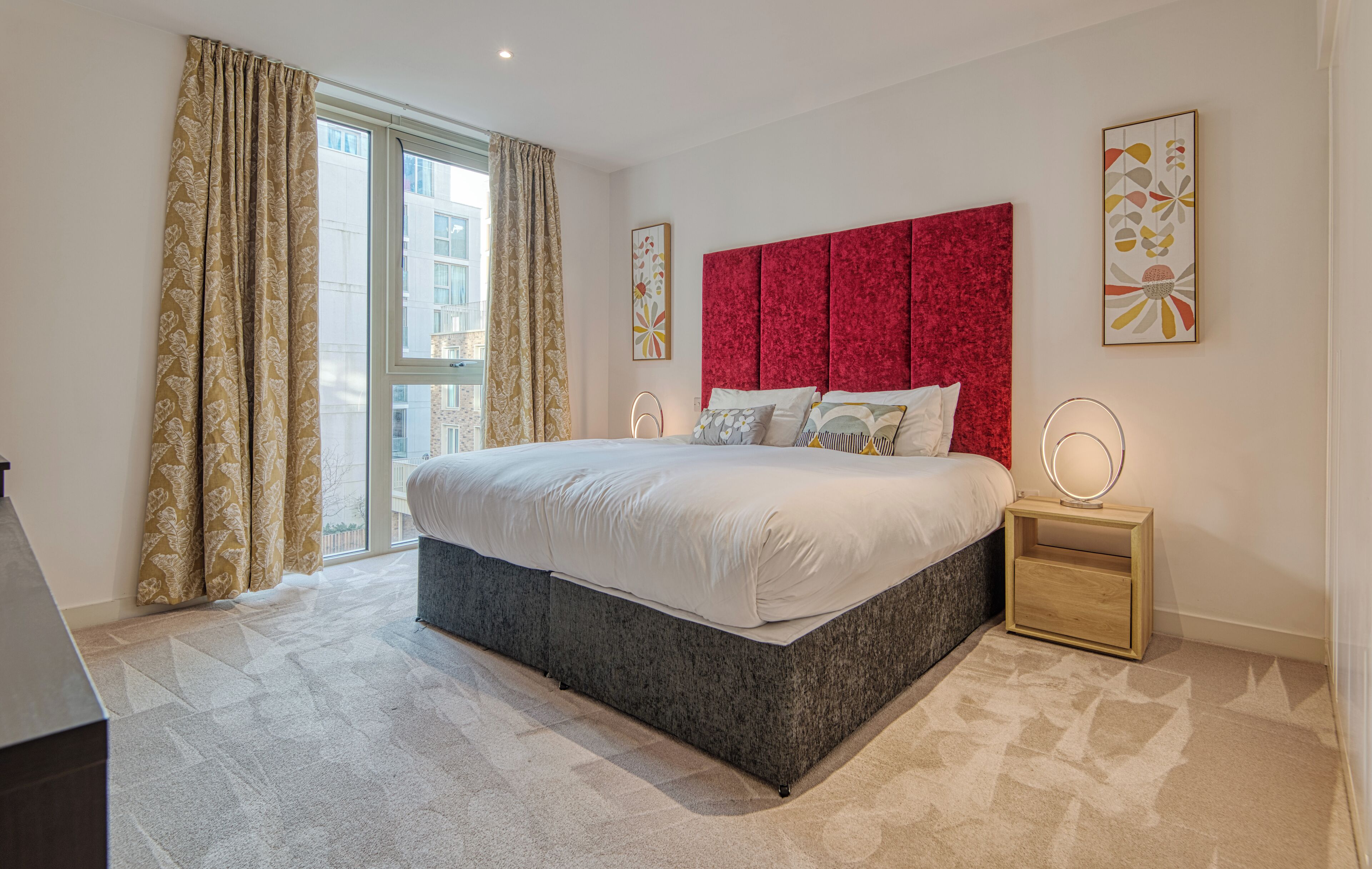 Un dormitorio moderno con una cama grande, cabecera roja y vista a la ciudad a través de la ventana.