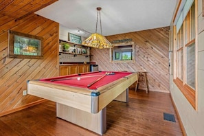 Une table de billard dans une pièce aux murs en bois et dotée d’une fenêtre.