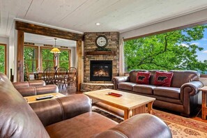 Un salon chaleureux avec des canapés en cuir, une cheminée et une grande fenêtre donnant sur les arbres.