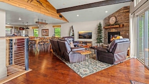 A spacious living area with a fireplace, leather sofas, a dining area, and a kitchen in the background.