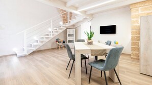 A modern interior with a staircase, a dining area with chairs and a table, and a TV mounted on the wall.