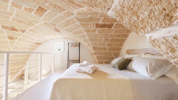 A bedroom with a stone ceiling, a bed with white linens, and a view of a balcony.