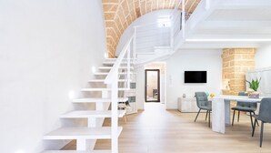 A modern interior with a white staircase, a dining area with chairs, a flat-screen TV, and a stone accent wall.