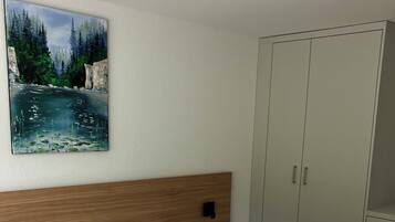 Ein Schlafzimmer mit Bett, Kopfteil, Nachttisch, Kleiderschrank und einem Bild an der Wand.