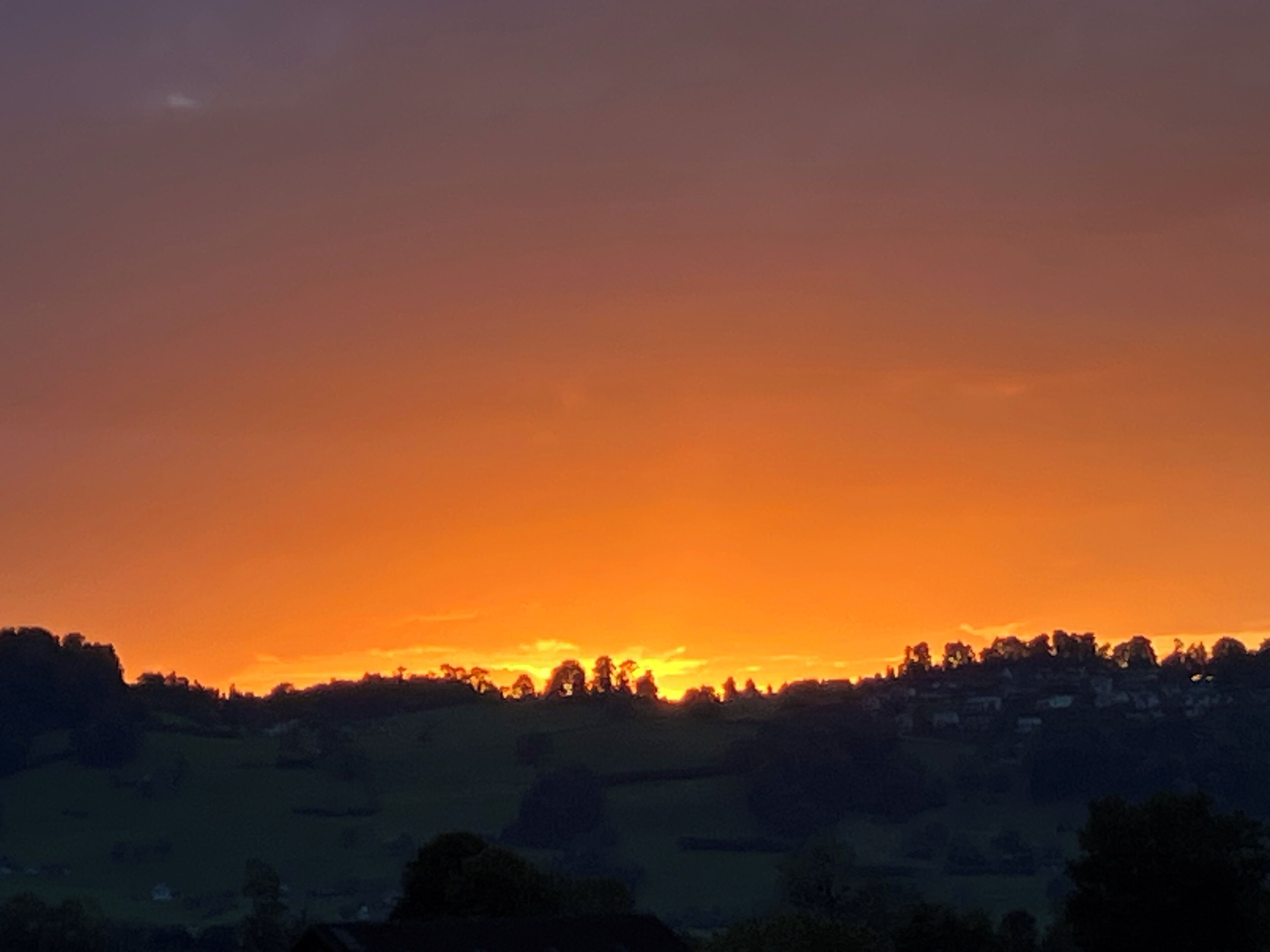Atardecer sobre un paisaje montañoso con siluetas de árboles y edificios.