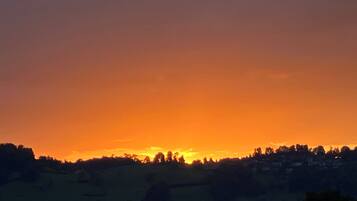 Atardecer sobre un paisaje montañoso con siluetas de árboles y edificios.