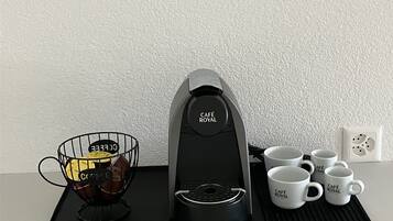Une machine à café, un panier métallique contenant des dosettes de café et quatre tasses blanches sur un plateau noir.