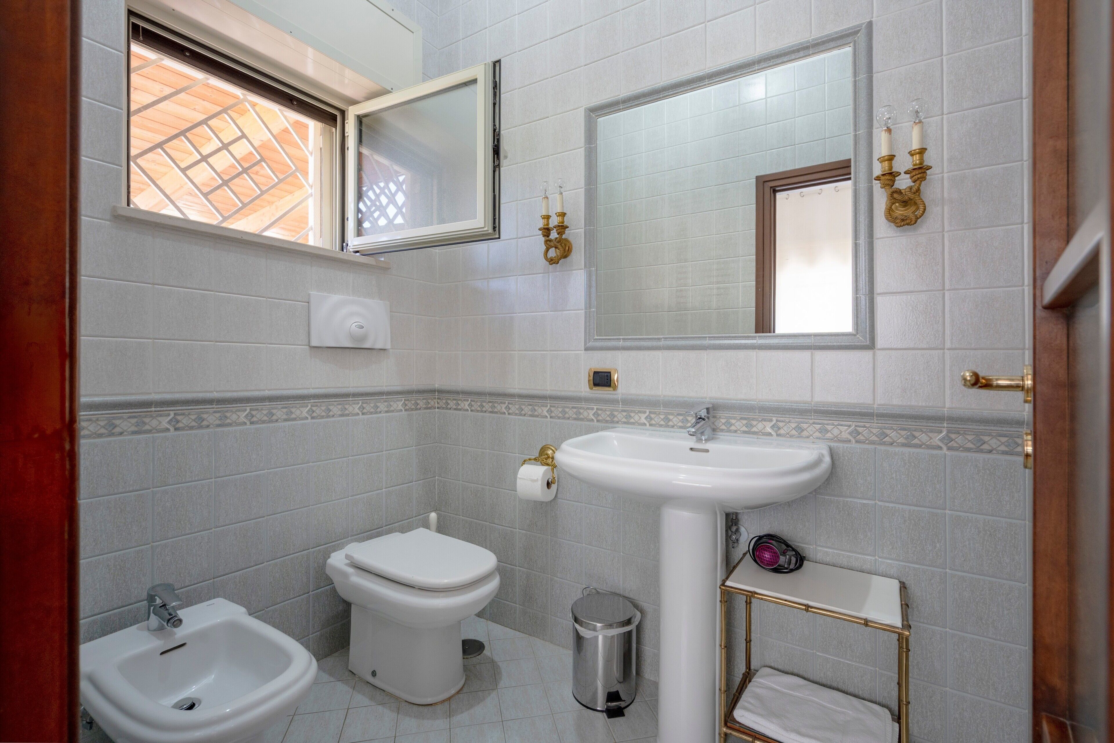 Ein Badezimmer mit einer Bidet-Einrichtung, Toilette, Waschbecken und einem Spiegel.