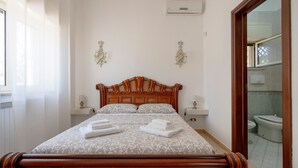 A neatly made bed with a wooden headboard, two bedside tables, and a bathroom visible through an open door.