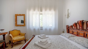 A bedroom with a bed, a chair, a mirror, and a window with curtains.