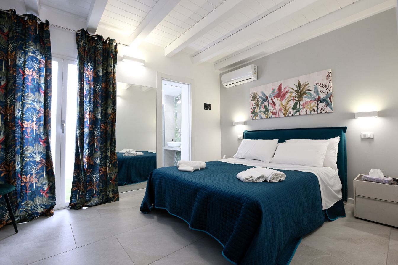 Una habitación de hotel con cama, mesita de noche, espejo y ventana con cortinas.