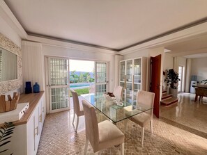 A spacious living area with a glass dining table, white chairs, and a view of a swimming pool. - Villa 'Casa Do Rei - Charneca' with Private Pool, Private Terrace and Wi-Fi (Charneca de Caparica)