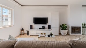 Una sala de estar moderna con un televisor de pantalla plana, gabinetes blancos, una mesa de centro y dos plantas en macetas.