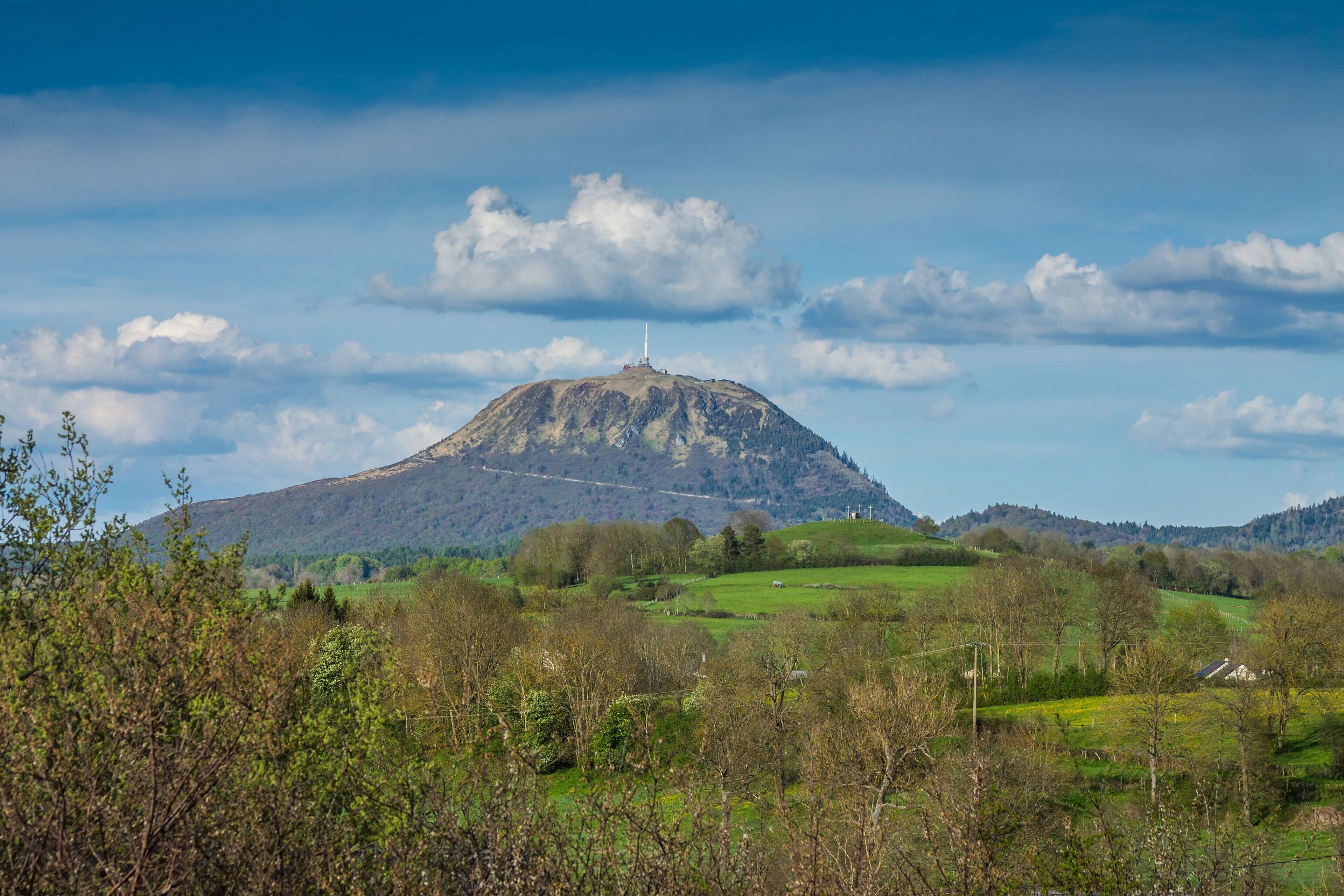A mountain with a tower, surrounded by green fields and trees.
