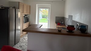 Una cocina moderna con un refrigerador de acero inoxidable, armarios de madera y vista a un jardín a través de una puerta de vidrio.