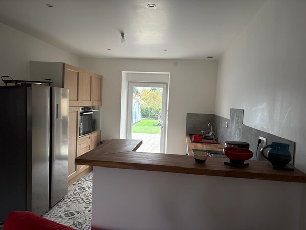 A modern kitchen with a stainless steel refrigerator, wooden cabinets, and a view of a garden through a glass door.