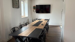 Un salón de conferencias con una larga mesa, sillas negras, un televisor montado y una ventana.