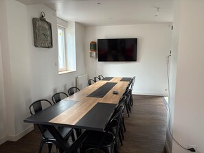 A conference room with a long table, black chairs, a mounted TV, and a window.