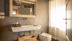 Ein Badezimmer mit einem Marmorwaschbecken, einer Holzkiste mit der Aufschrift 'BUITONI', einem weißen Bidet und einem Spiegel mit einer Chandelüster.