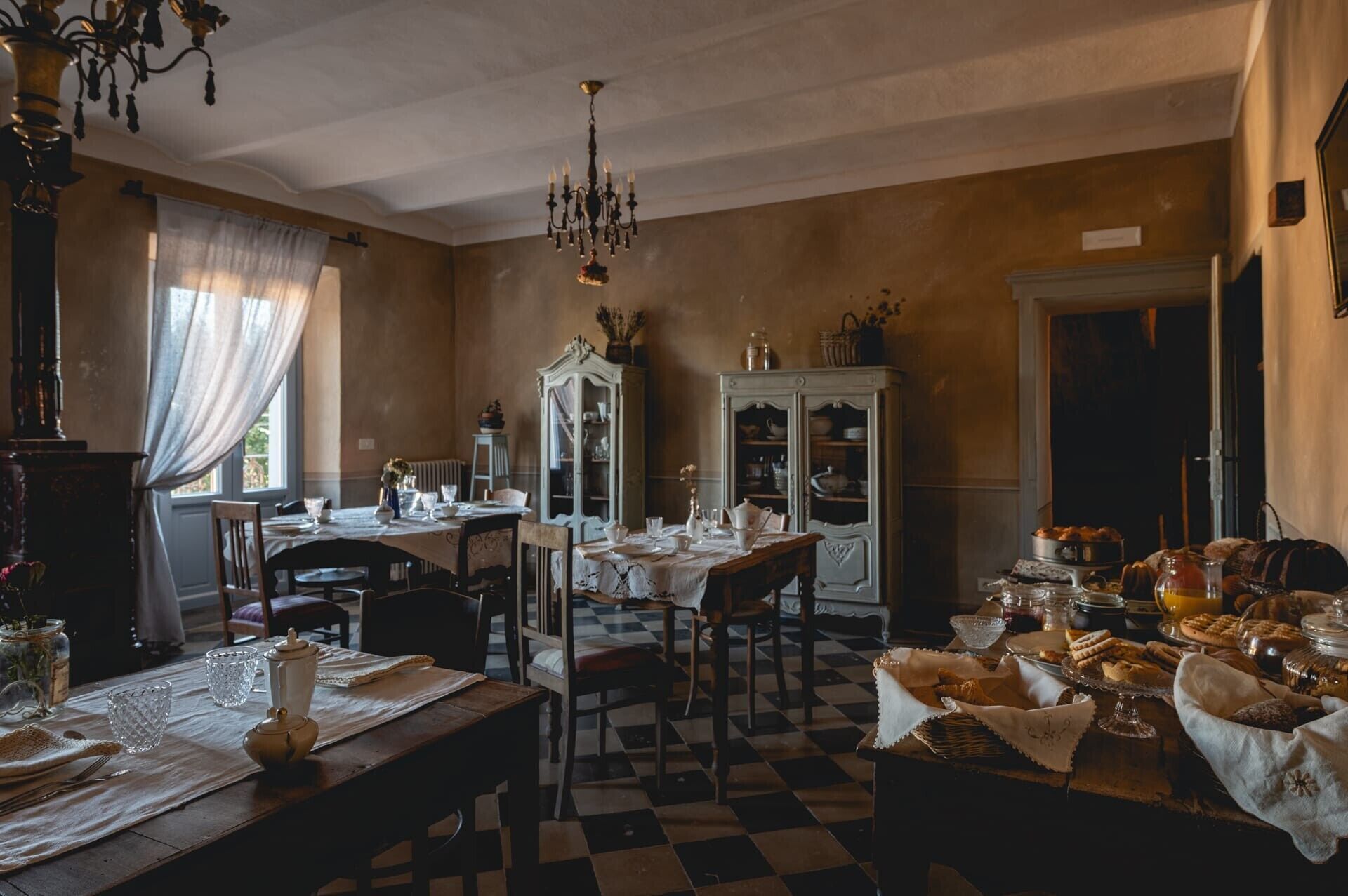 A dining room with a checkered floor, a chandelier, and a cabinet with dishes.