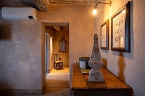 Un couloir avec un banc en bois, une sculpture en pierre, des tableaux encadrés et un miroir.