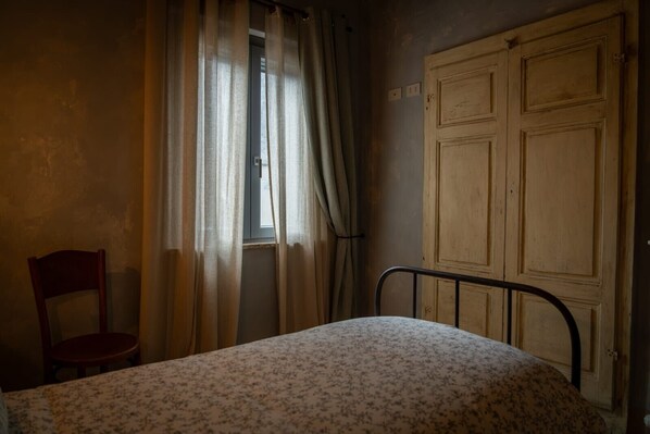 Una habitación con una cama, una silla, un ventanal con cortinas y un armario de madera.