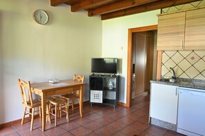 Un comedor con una mesa y sillas de madera, un televisor sobre un mueble bajo y una cocina con lavavajillas.
