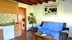 Sala de estar con sofá, mesa de centro, lavadora, planta en maceta y área de cocina con alacenas y lavavajillas.
