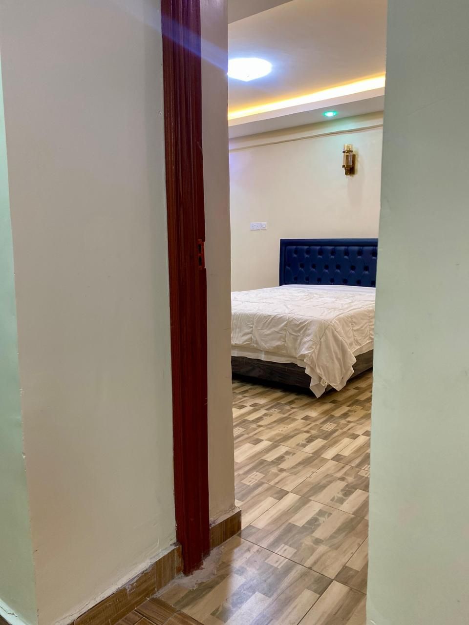 A room with a wooden floor, a bed with a blue headboard, and a red door.