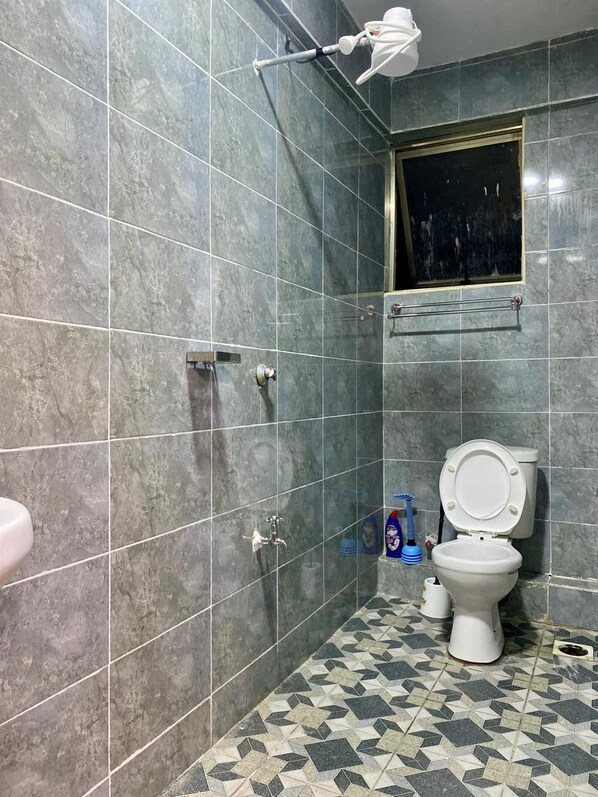 A bathroom with grey tiled walls, a white toilet, a window, and a shower area. - Abhi El Mara Suites Rongo (Rongo)