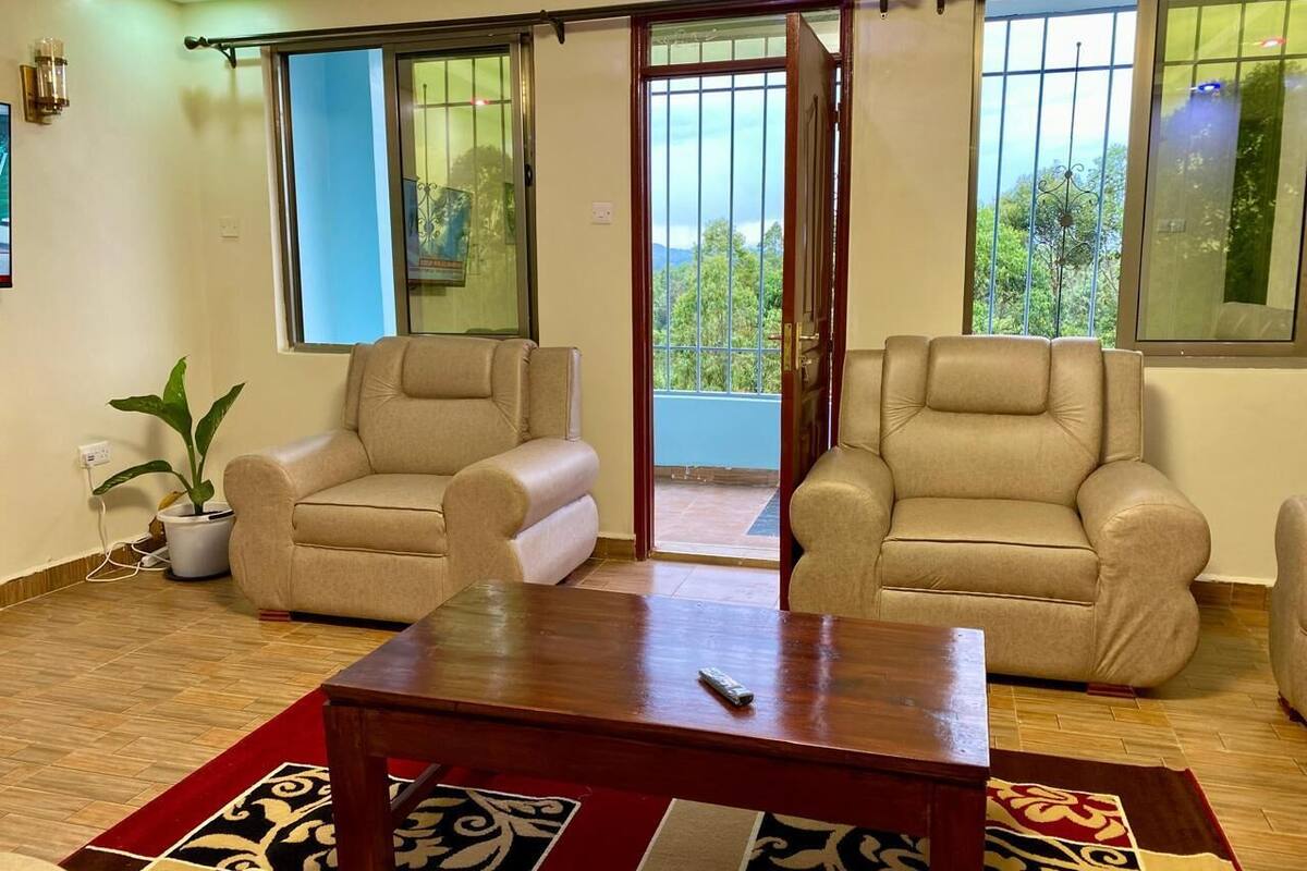 A living room with two beige armchairs, a wooden coffee table, and a red patterned rug.