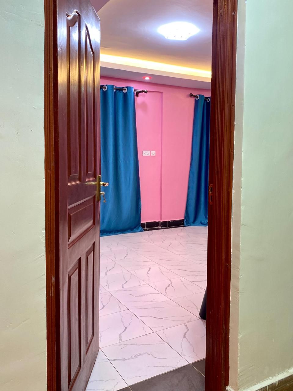 Una habitación con puerta de madera, paredes rosas y cortinas azules.