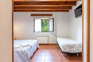 A small room with two beds, a window with curtains, a radiator, and a TV mounted on the wall.
