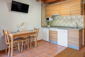 A compact kitchen with a dining table, chairs, a microwave, a dishwasher, and a TV mounted on the wall.