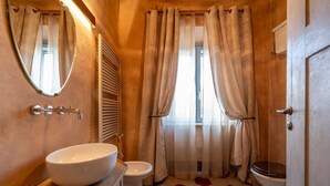 Een badkamer met een rond wastafel, twee toiletten, een spiegel en een raam met gordijnen.