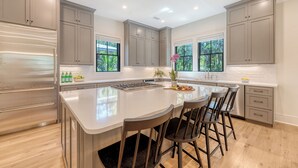 A modern kitchen with a large island, grey cabinetry, and a view of greenery outside. - New Build with pool in central neighborhood (Kiawah Island)