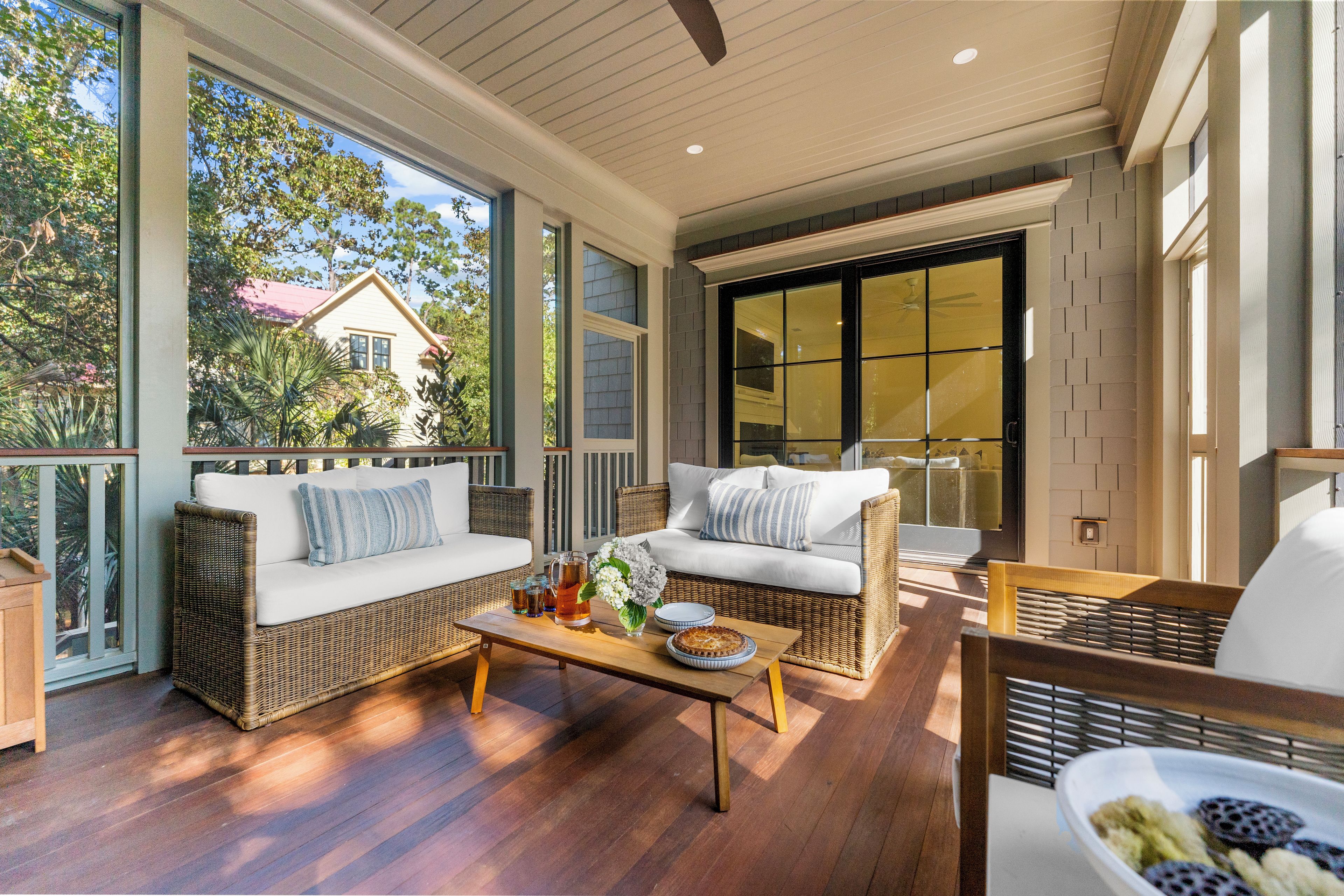 A spacious balcony with wicker furniture, a wooden coffee table, and a view of a house and trees.