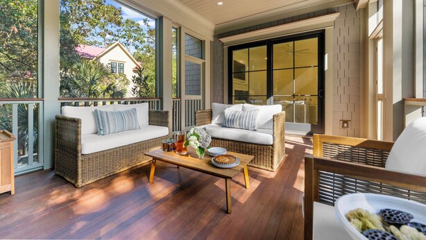 A spacious balcony with wicker furniture, a wooden coffee table, and a view of a house and trees. - New Build with pool in central neighborhood (Kiawah Island)