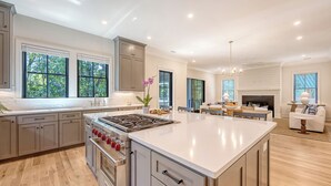 A modern kitchen with a large island, built-in oven, and a dining area with a fireplace. - New Build with pool in central neighborhood (Kiawah Island)