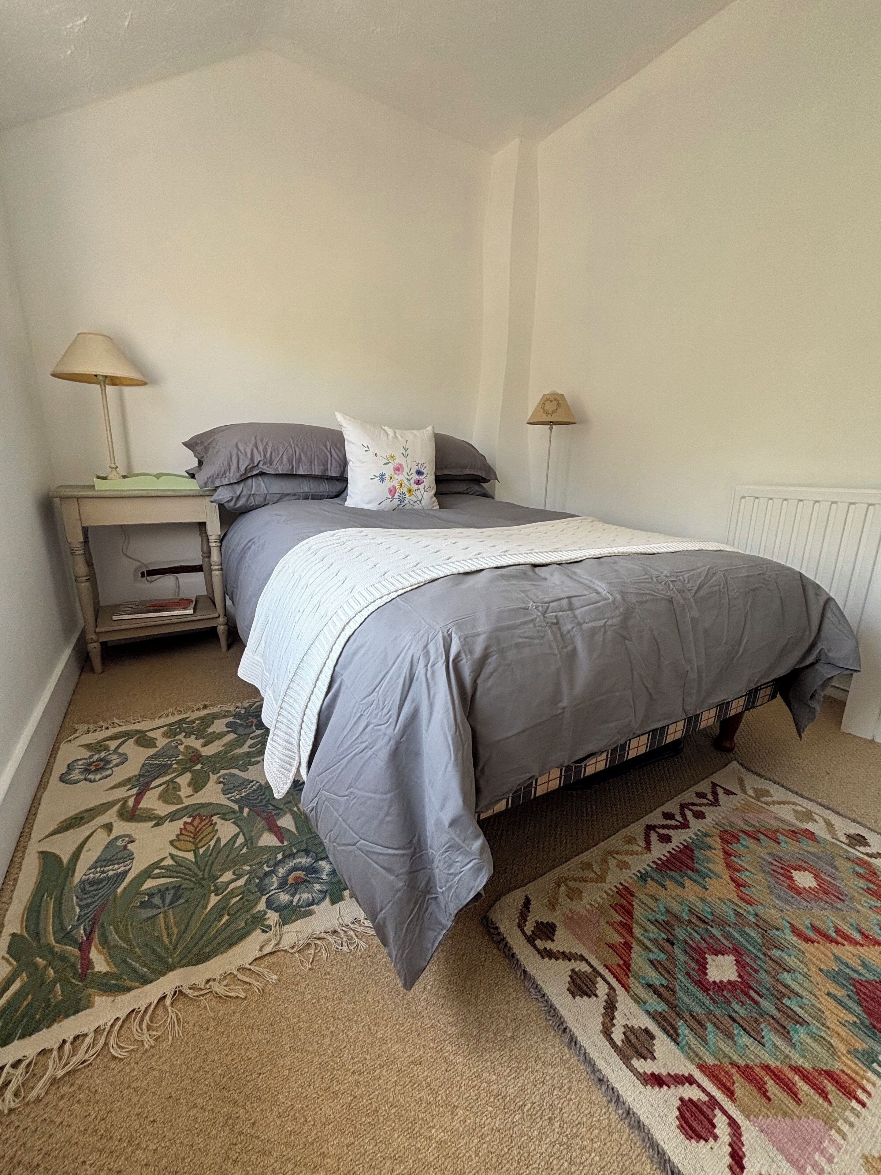 A bedroom with a bed, two bedside tables, a nightstand, a patterned rug, and a radiator.